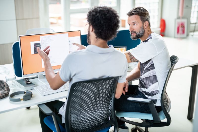 Zwei Männer arbeiten gemeinsam an einem Projekt und zeigen auf einen Monitor